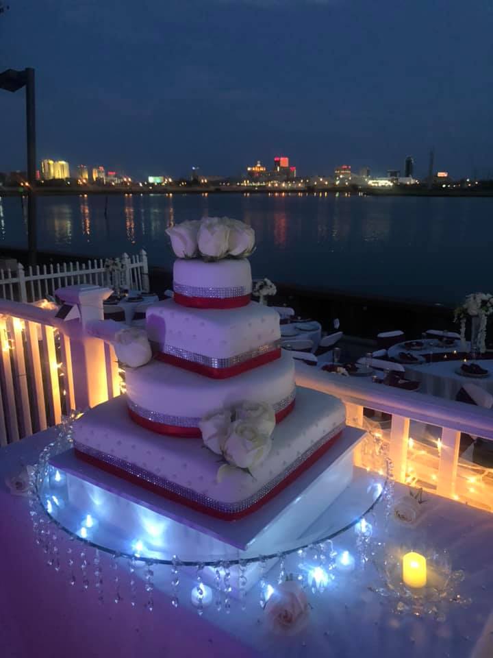 Four-tier wedding cake with red ribbons on a waterfront balcony at night with the city skyline in the background