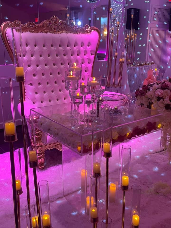 Romantic party setup with pink and purple lighting, gold-framed tufted loveseat, glass table, and floating candles