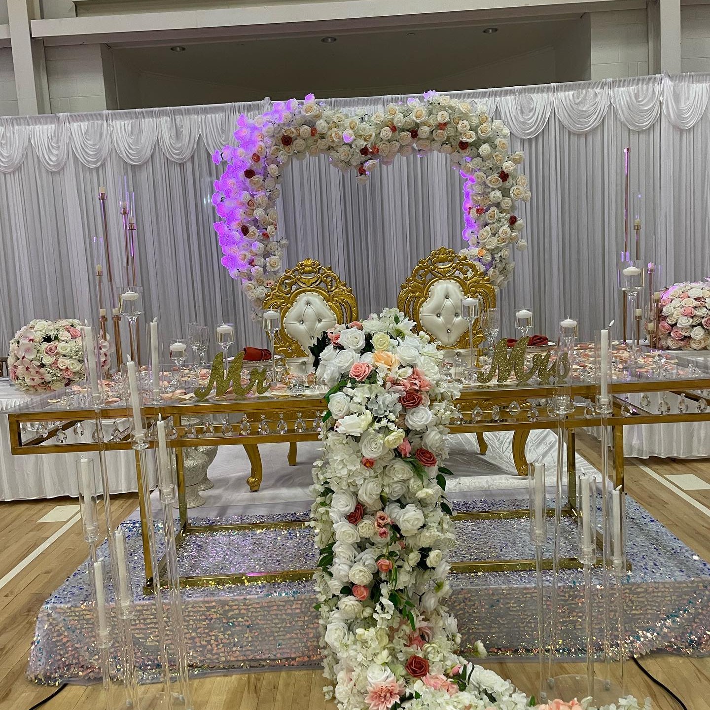Heart-shaped floral arch in cream and blush above a wedding sweetheart table with cascading floral runner