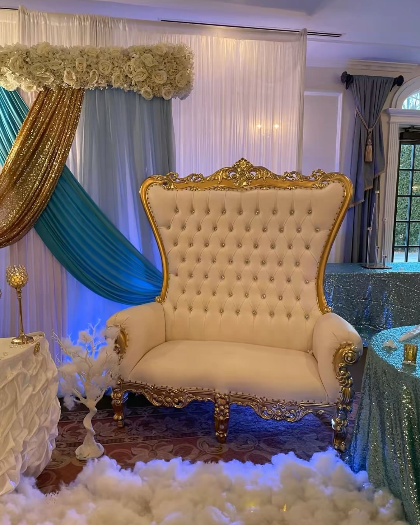 Single ornate gold-framed throne loveseat under a white floral arch with teal and gold drapes
