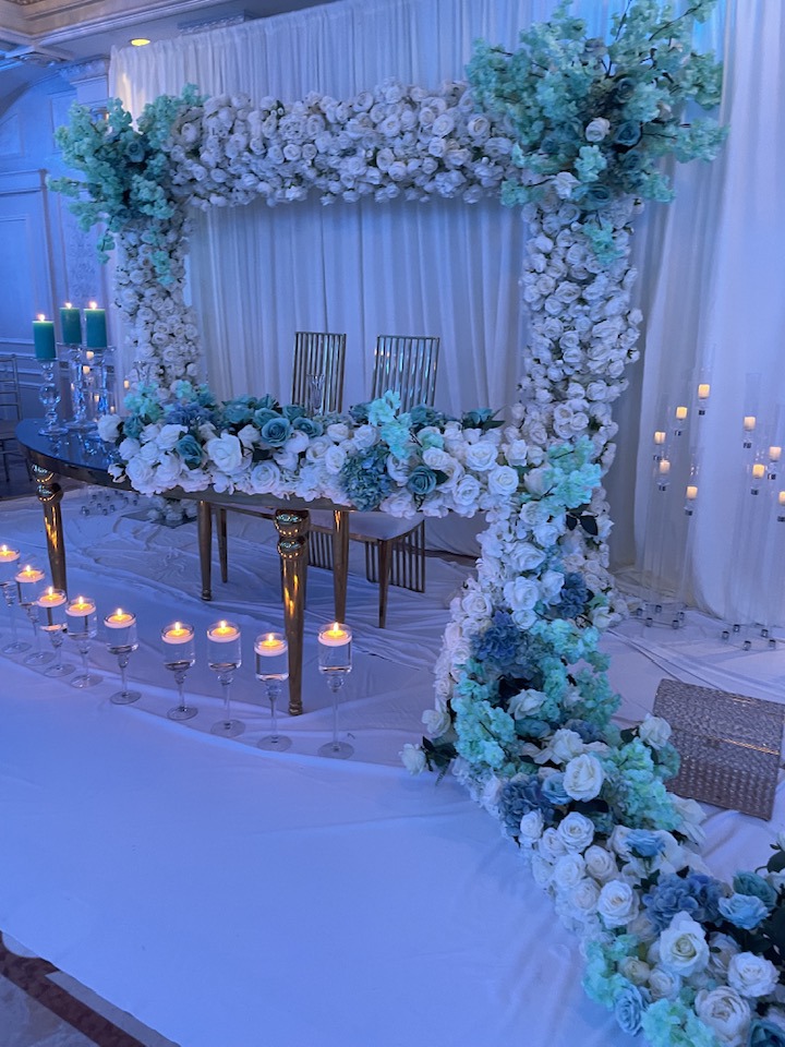 Square floral frame in white, sage, and powder blue florals surrounding a sweetheart table with floating candles