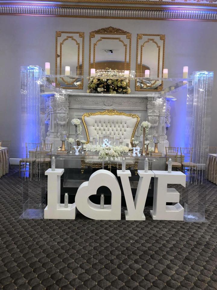 White and gold ballroom wedding with LOVE letter sign and floating candles in front of a mirrored fireplace