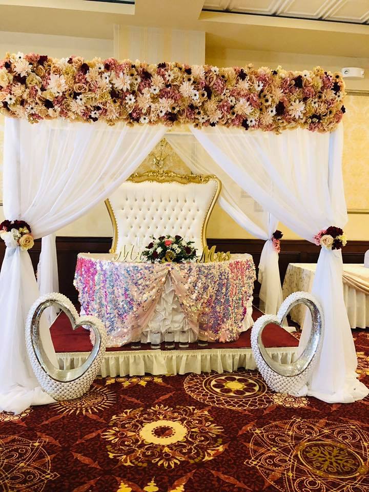 Wedding sweetheart table with burgundy and cream floral valance, sequin tablecloth, and white draped backdrop