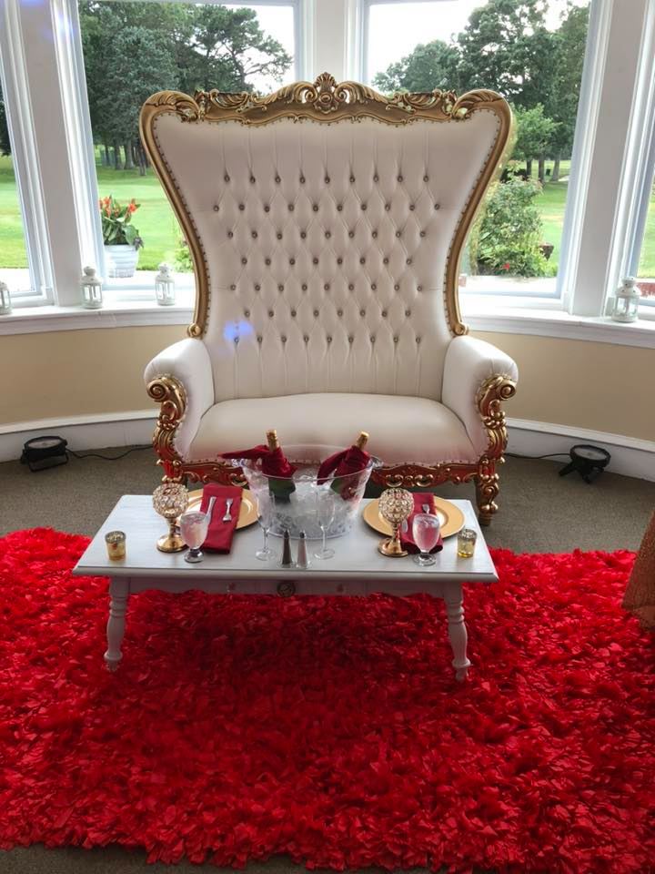 Gold-framed cream throne loveseat on red shag rug with white coffee table, champagne bucket, and red accents